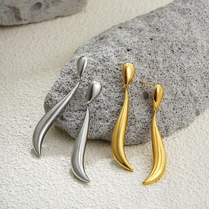 Detailed view of long curved teardrop earrings in gold and silver on natural grey stone