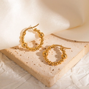 Detailed macro view of 18k gold-plated beaded hoop earrings on elegant marble background