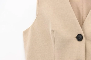 Dettaglio dello scollo a V, del tessuto beige e del bottone in resina nera sul vestito