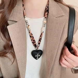 Detail of leopard print necklace with matte black heart pendant and silver cross icon