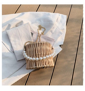 Detail view of woven straw bucket bag with pearl handle and metal chain on white blazer