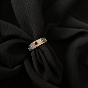 Macro detail of silver floral embossed ring with a red gemstone on black fabric