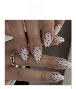Close-up of almond-shaped fake nails with white base and black polka dot pattern
