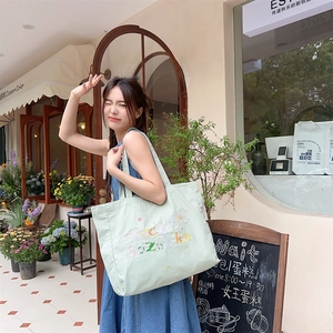 Détail du sac cabas en toile vert menthe avec broderie lucky porté par un mannequin en extérieur