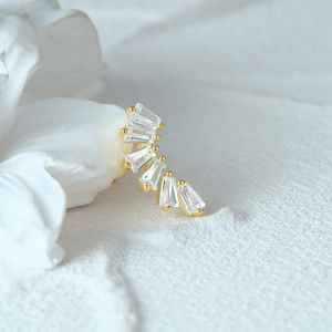 Macro shot of curved gold moon earring with five baguette-cut crystals on a white petal