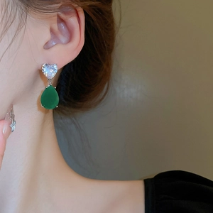 Close-up of heart zircon and green teardrop earring worn on ear with soft lighting