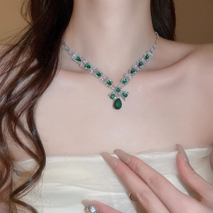 Close-up of luxury silver necklace with green teardrop pendant worn by model