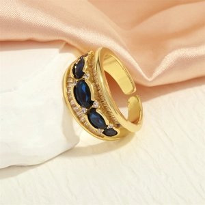 Detail of 18K gold-plated X-shape ring with oval blue gemstones on pink silk fabric