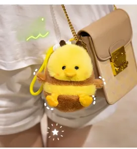 Plush bee-duck hybrid charm accessory shown hanging on a stylish beige chain handbag