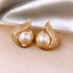 Macro detail of gold-plated mermaid pearl earrings with zircon on silk fabric