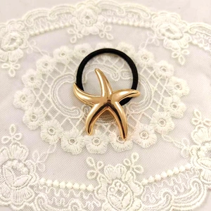 Macro detail of a polished gold starfish hair tie accessory on elegant white lace fabric