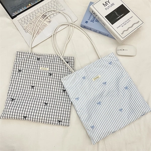 Detail of checkered and striped canvas tote bags with delicate bow embroidery and long straps