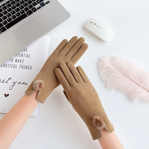 Close-up of brown faux suede winter gloves with plush pom pom cuffs on a white desk