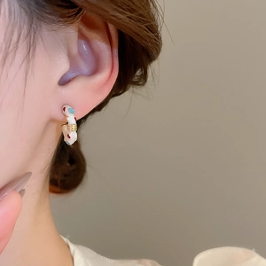 Close-up of white enamel C-shaped earring with red and blue spots worn by a model