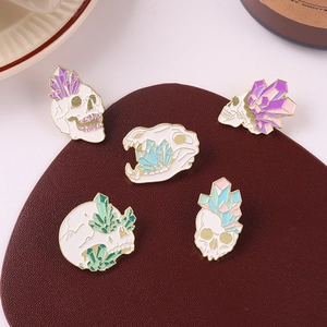 Detailed view of skull and crystal enamel pins on a dark textured background