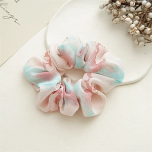 Detail of pink and blue floral tie-dye scrunchie on a ceramic tray with soft shadows