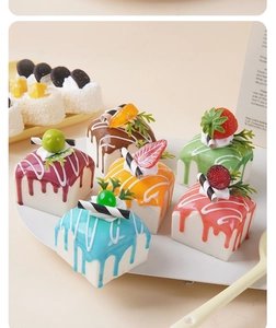 Close-up of assorted PU realistic cake models with colorful dripping glaze and fruit toppings