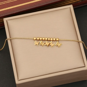 Detail of a gold butterfly bracelet with small beads and box chain on a beige box