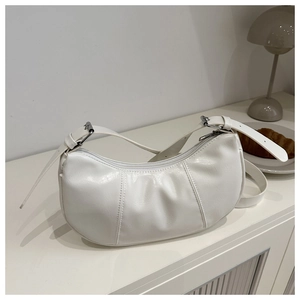 Detail of white pleated crescent underarm bag with adjustable silver buckle on a table