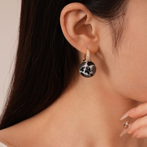 Close-up of model wearing gold zircon C-shape hoop earrings with black marble resin ball