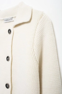 Détail de l'encolure du cardigan en maille blanche et de l'étiquette BBWM WOMAN sur le col