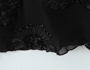 Detailed macro view of black mesh fabric with 3D floral accents and wavy edge finish