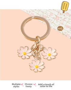 Detailed close-up of three pink daisy charms on a golden alloy keychain for bags