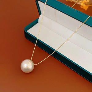 Macro shot of large pearl pendant with golden snake chain on a green velvet jewelry box