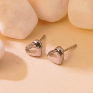 Macro shot of silver heart stud earrings made of polished steel on a natural stone surface