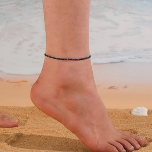 Close-up of minimalist beaded turquoise anklet on ankle with beach and ocean background