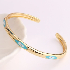 Verstellbares goldenes Manschettenarmband mit blauem Emaille-Auge auf weißem Porzellan