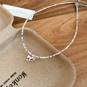 Detail of beaded necklace with pink enamel rocking horse pendant on a rustic tray