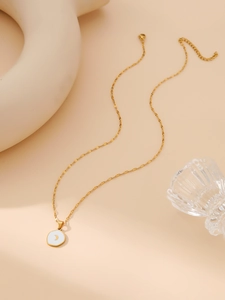 Close-up of a minimalist gold necklace with a round white enamel moon pendant