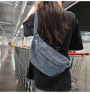 Detailed back view of a blue denim crossbody bag worn by a model in a shopping mall