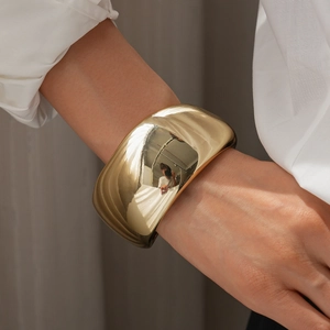 Close-up of a wide polished gold metal cuff bracelet worn by a model in a white shirt