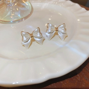 Macro view of gold-plated bow earrings with white pearlescent finish on a ceramic plate