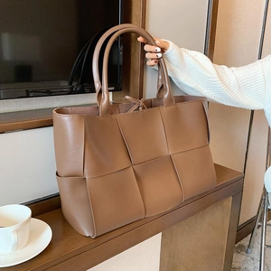 Brown woven leather tote bag with large handle design for women on a wooden table
