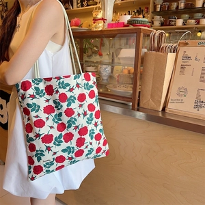Grand sac cabas en toile à fleurs avec motif de roses rouges porté à l'épaule au café