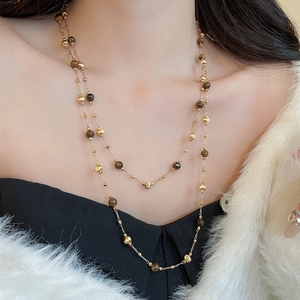 Close-up of double-layered gold necklace featuring tiger eye beads and metal accents