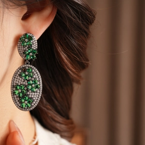 Macro detail of vintage floral oval earrings with emerald green stones and white zircons