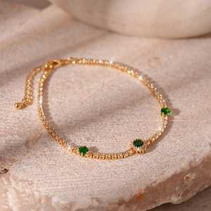 Detailed macro view of a gold-plated tennis bracelet with green emerald and white cubic zirconia