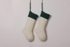 Detail of two cream white knitted Christmas stockings with dark green cuffs on a wall