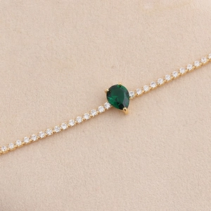 Detail van gouden ketting met peervormige smaragd hanger en zirkonia-accenten