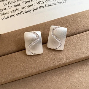 Close-up of matte silver rectangular stud earrings with S-curve zircon inlays