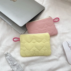Flat lay of quilted heart mini pouches in pink and yellow with laptop on white fabric