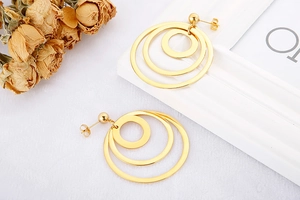 Detail of triple-linked golden geometric circle stud earrings on white fabric backdrop