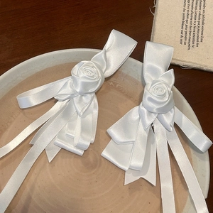 Detailed close-up of white rose hair clips with ribbon tassels on a ceramic dish