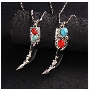 Detailed view of two ethnic wolf tooth pendants with red and turquoise gemstone inlays