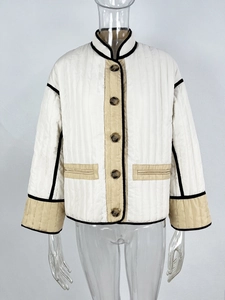 Detail of a white quilted jacket featuring beige trim, black piping, and brown buttons