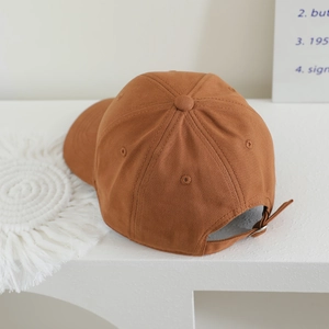 Detail of adjustable metal buckle and strap on back of tan cotton baseball cap